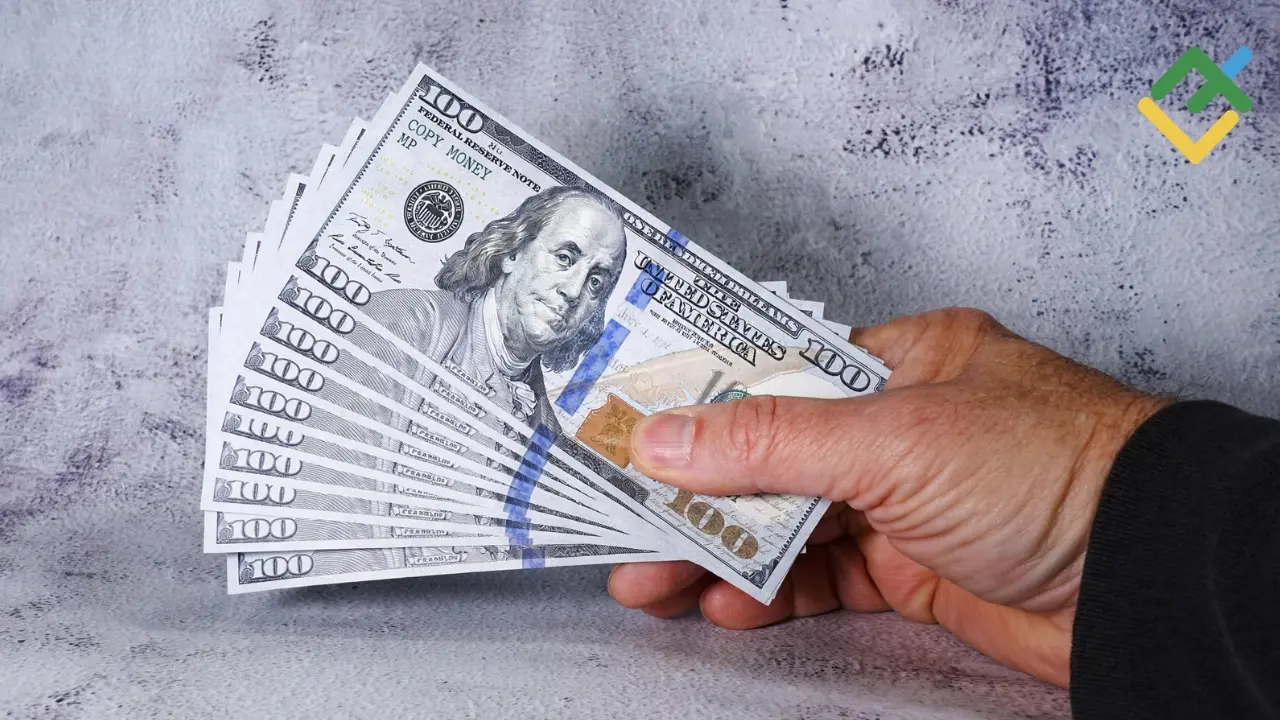 Hand holding fanned stack of $100 prop money bills demonstrating how to start investing with $100 in 2026